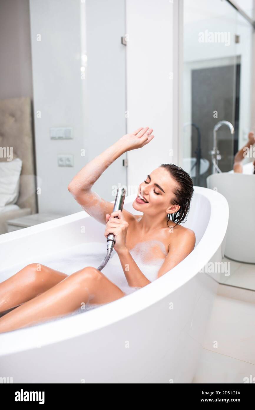 Una joven canta una canción sosteniendo el mango de la ducha en las manos  en espuma en el baño Fotografía de stock - Alamy