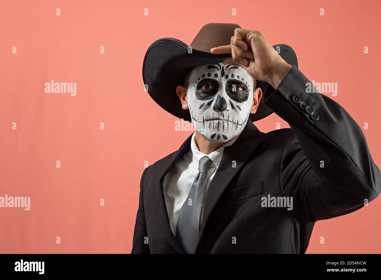 Hombre disfrazado de catrin con traje negro y sombrero marrón, sosteniendo  su sombrero con una mano, posando con un fondo liso Fotografía de stock -  Alamy