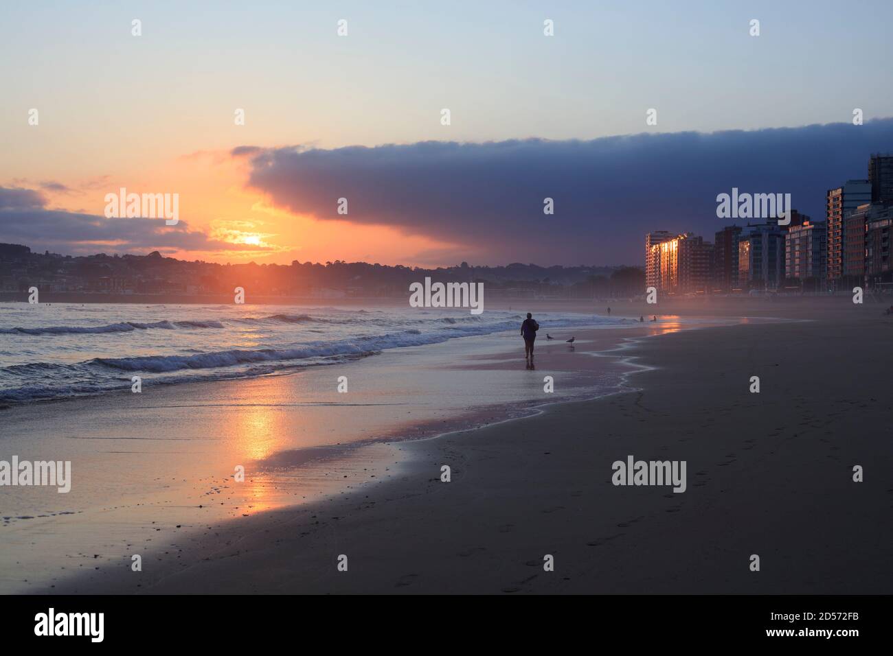 Un hombre camina a lo largo de la playa de San Lorenzo durante el amanecer en la ciudad de Gijón. Mar Cantábrico. Asturias. España Foto de stock