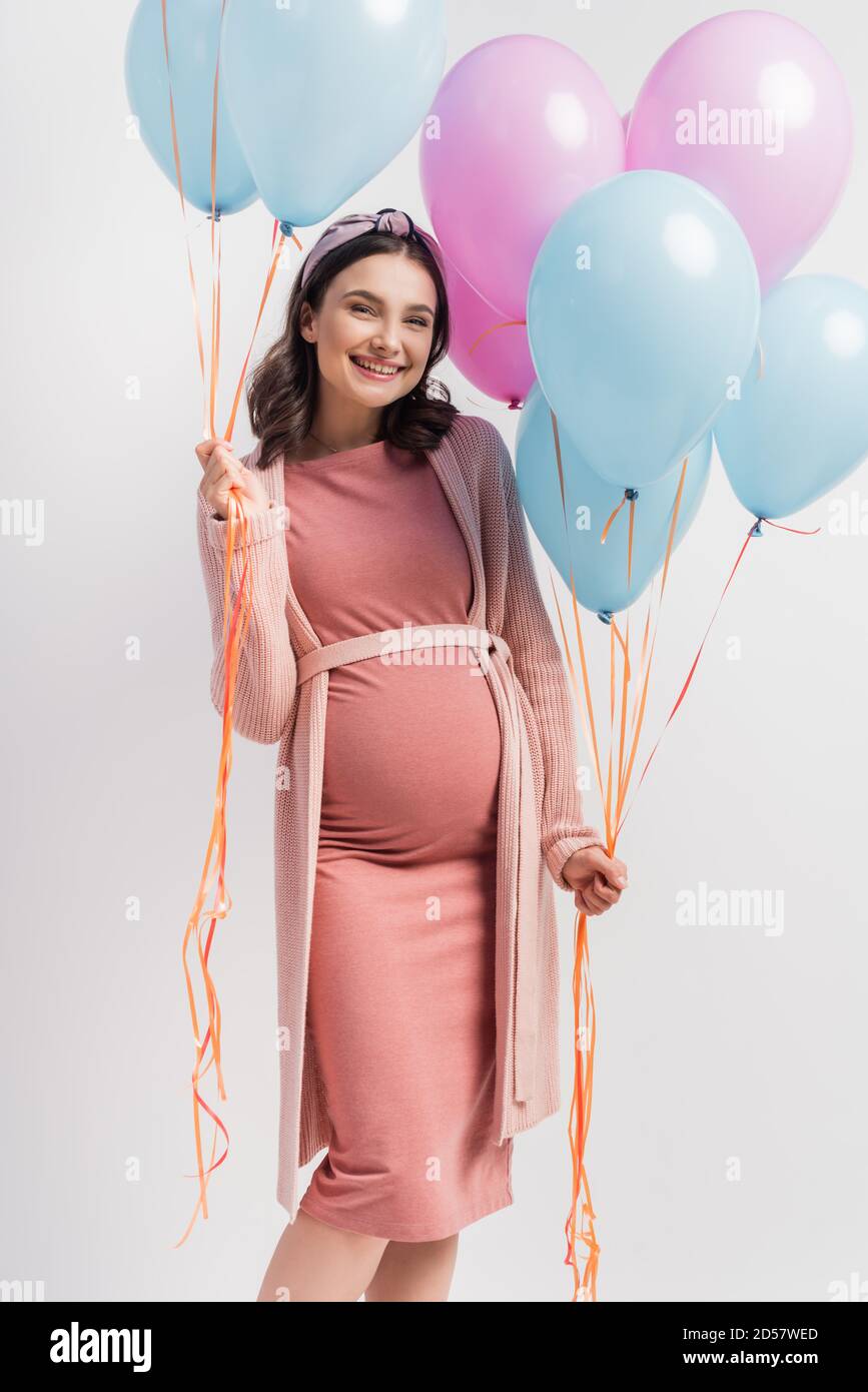 mujer alegre y embarazada con vestido rosa sosteniendo globos