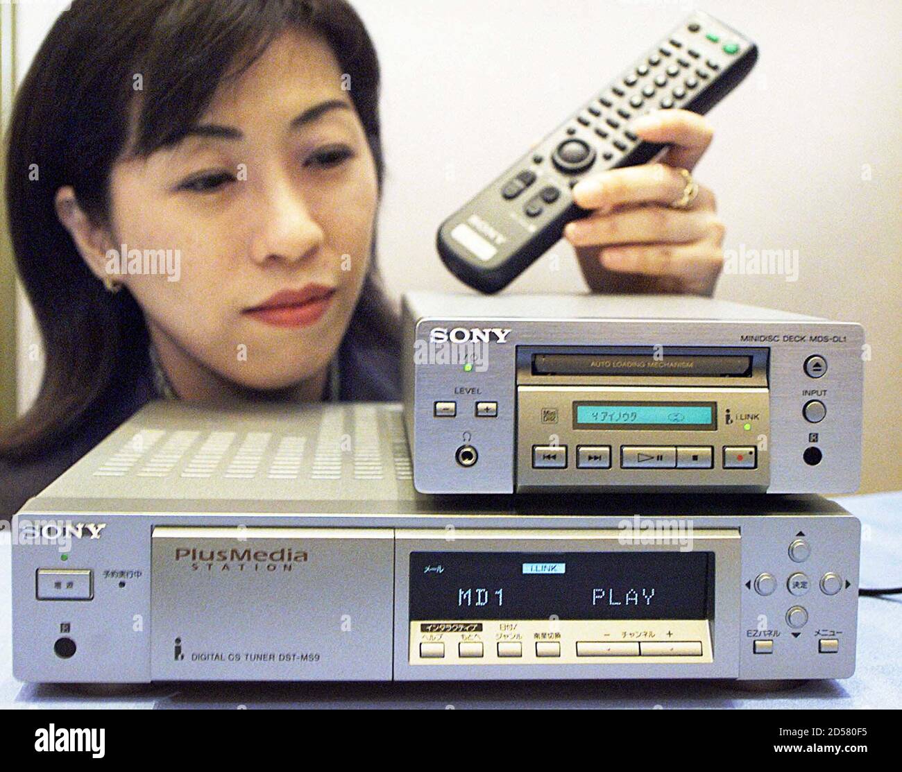 Kuriko Takeshima, empleada de Sony Corp, muestra su nuevo receptor de transmisión digital vía satélite de comunicación (CS) DST-MS9 (inferior) de marzo de 25, que permite a los suscriptores recibir nueva programación de transmisión de datos que ofrecerá SkyPerfect TV. En Japón, y el nuevo reproductor/grabador de mini disco modelo MDS-DL1 (top). Los suscriptores de este canal podrán elegir y descargar su música favorita en un mini disco conectando DST-MS9 y MDS-DL1. El nuevo receptor llegará al mercado el 20 de mayo y se venderá por 50,000 yenes ($424) y el nuevo mini reproductor/grabador el 21 de junio por 59,000 yenes ($500). ST/CC Foto de stock