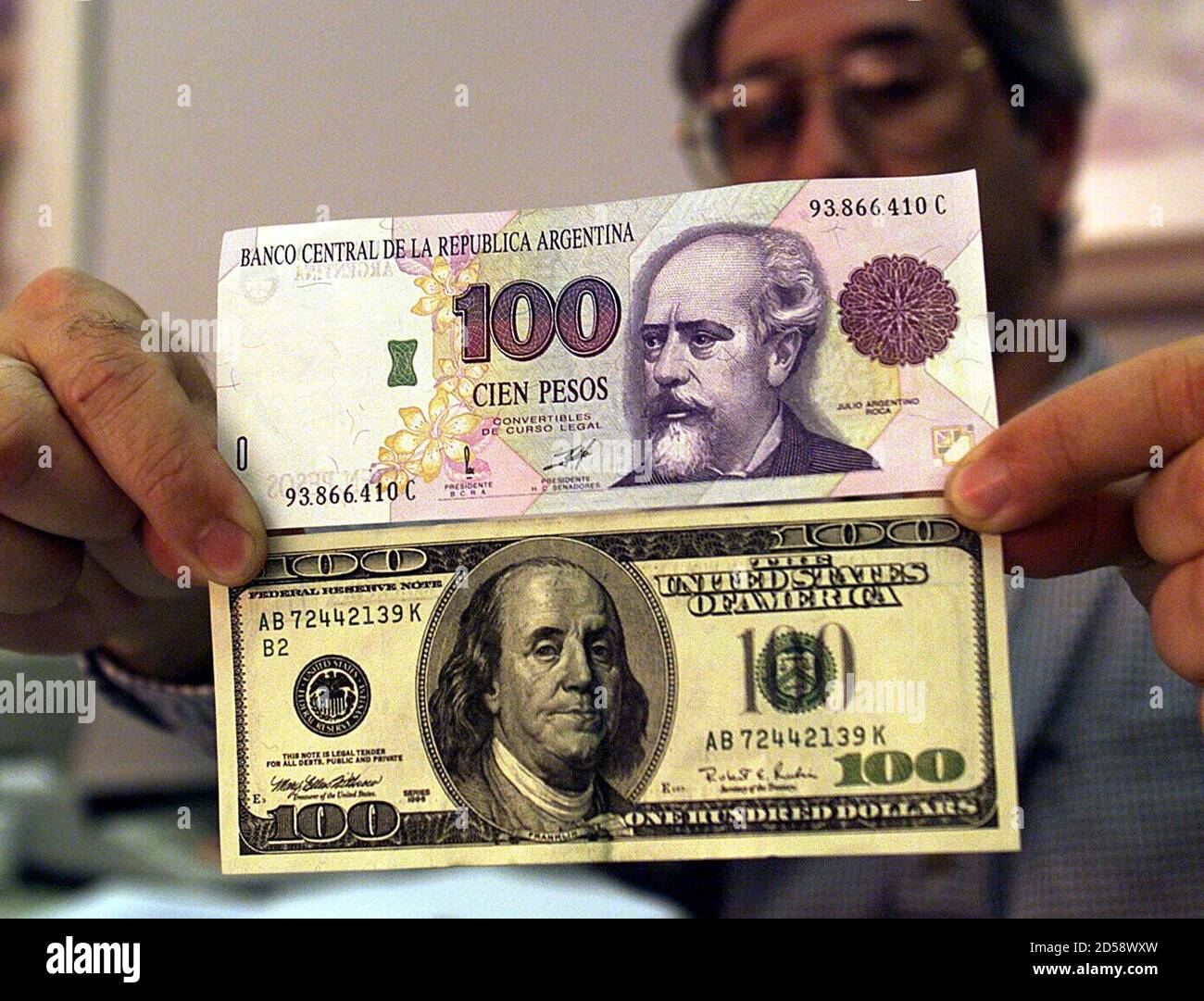 Un economista argentino tiene un proyecto de ley de $100 junto con un  billete de 100 pesos argentinos de exactamente el mismo valor en la  economía local, enero de 19. Bajo el