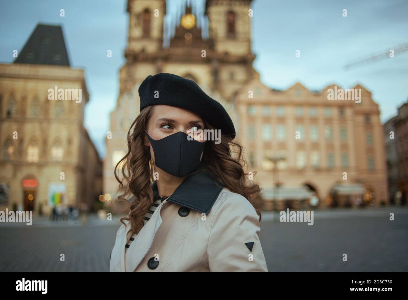 Hola otoño. Mujer de mediana edad moderna en gabardina beige y bereta negra con máscara negra en la Plaza de la Ciudad Vieja de Praga. Foto de stock
