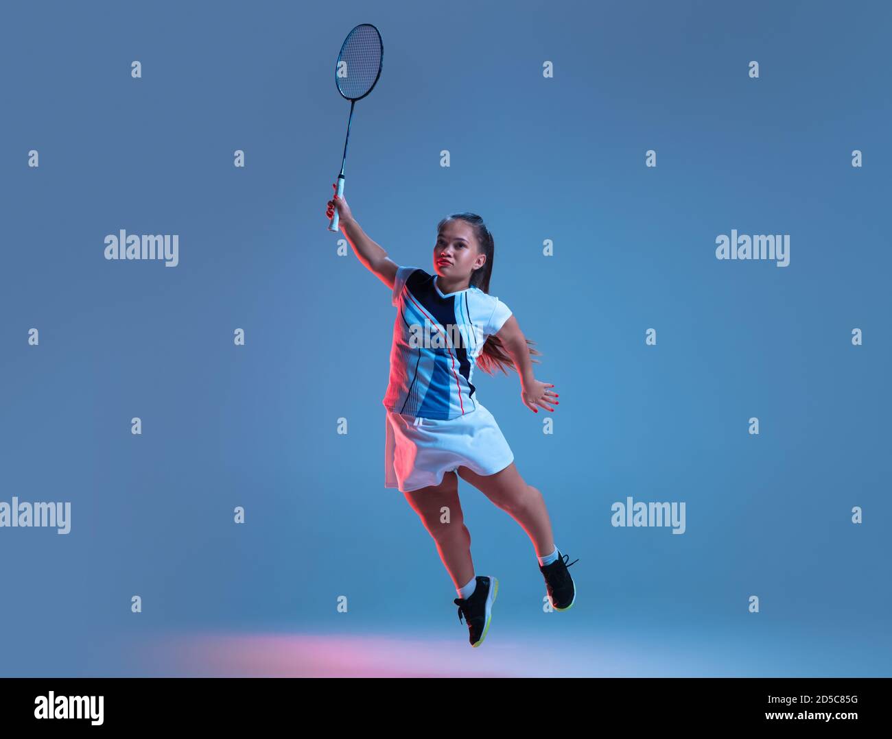 Ganador. Hermosa mujer enana practicando en badminton aislado sobre fondo azul en luz de neón. Estilo de vida de personas inclusivas, diversidad y equilidad. Deporte, actividad y movimiento. CopySpace. Foto de stock