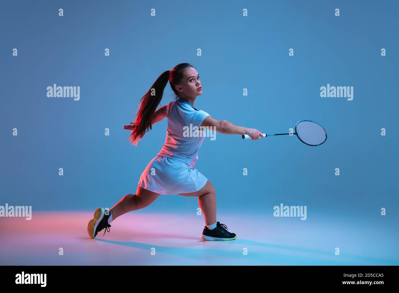 Ganador. Hermosa mujer enana practicando en badminton aislado sobre fondo azul en luz de neón. Estilo de vida de personas inclusivas, diversidad y equilidad. Deporte, actividad y movimiento. CopySpace. Foto de stock