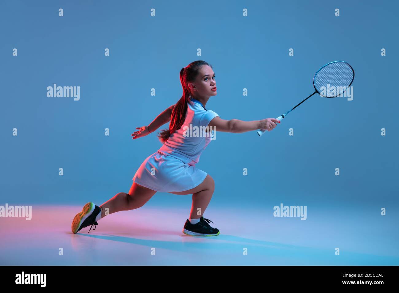 Ganador. Hermosa mujer enana practicando en badminton aislado sobre fondo azul en luz de neón. Estilo de vida de personas inclusivas, diversidad y equilidad. Deporte, actividad y movimiento. CopySpace. Foto de stock