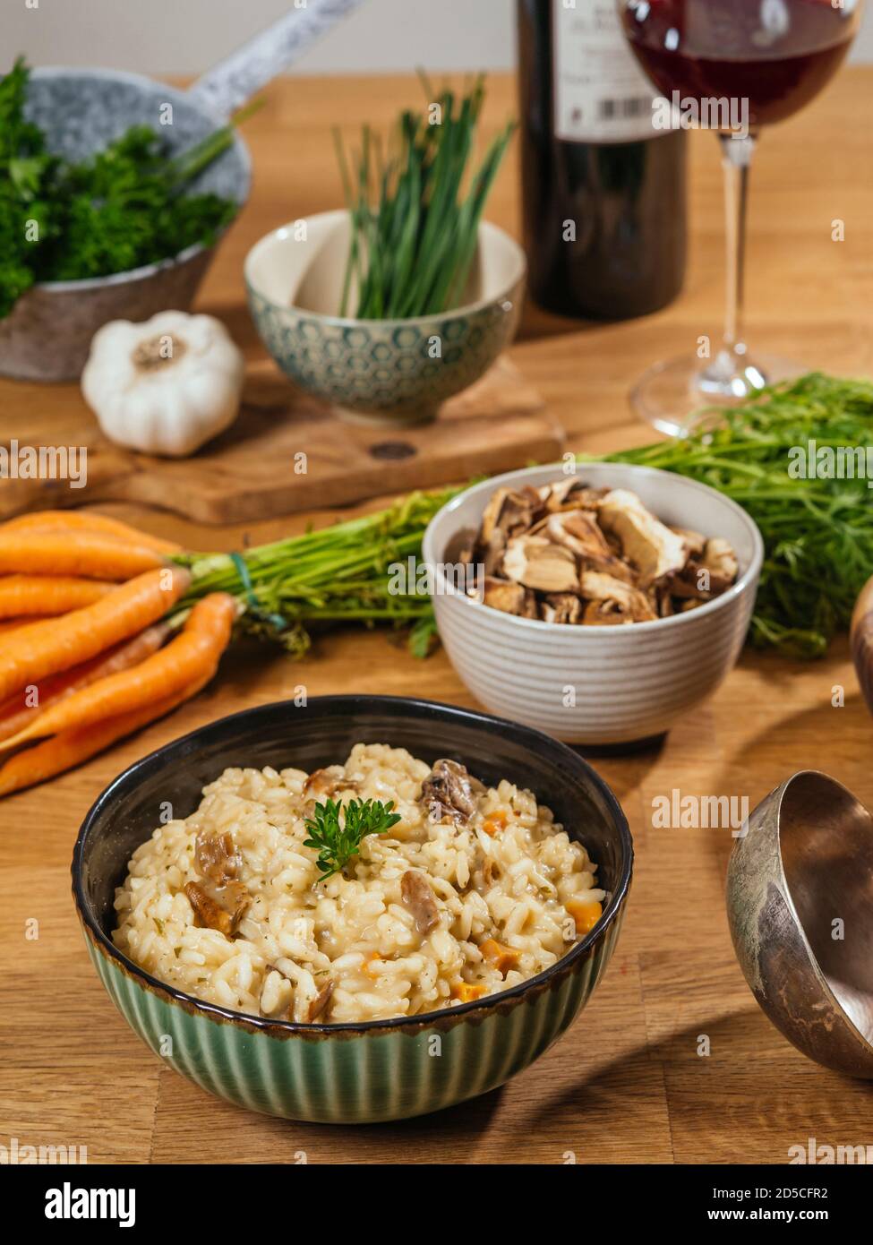 Cuenco de risotto sobre una mesa con ingredientes, setas, ajo, zanahorias y una copa de vino. Foto de stock