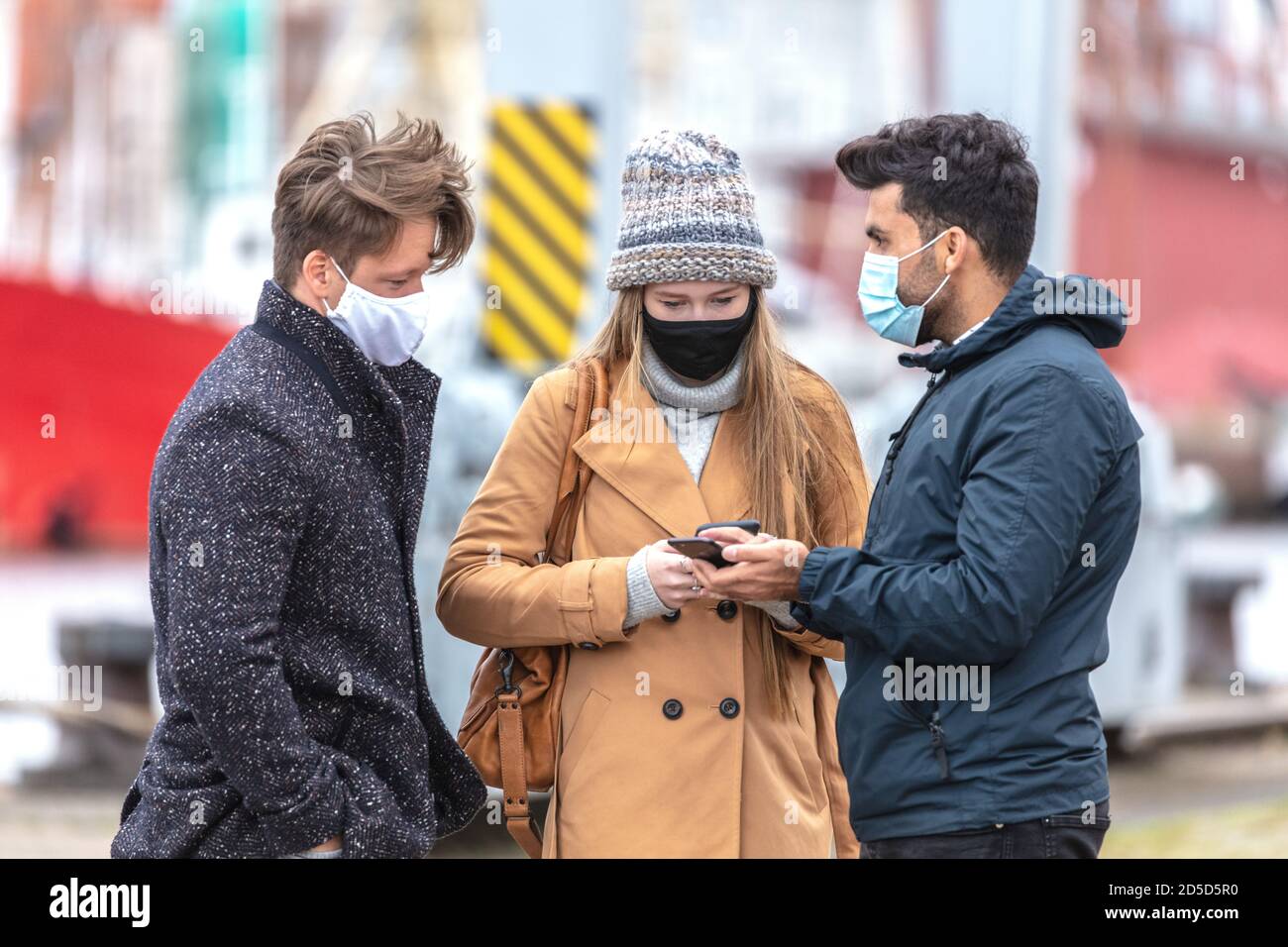 Zwei Männer und eine Frau in Corona-Zeit, mit alltäglichen Masken, in der kalten Jahreszeit in der Stadt unterwegs. Foto de stock