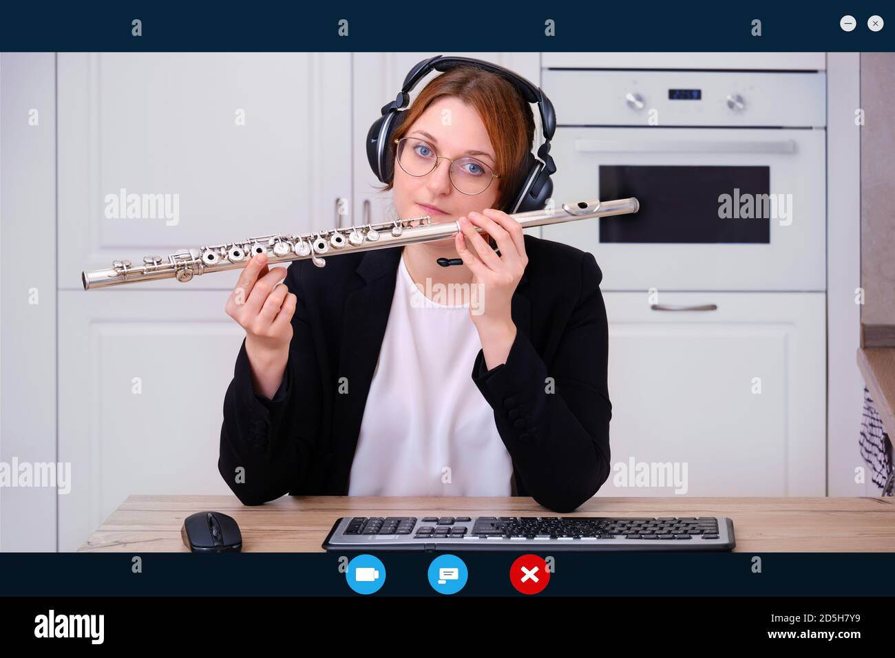 Un profesor en un traje de negocios y auriculares sostiene una flauta  durante una clase de música en línea. Una pantalla de una cámara web con el  aprendizaje en línea de la