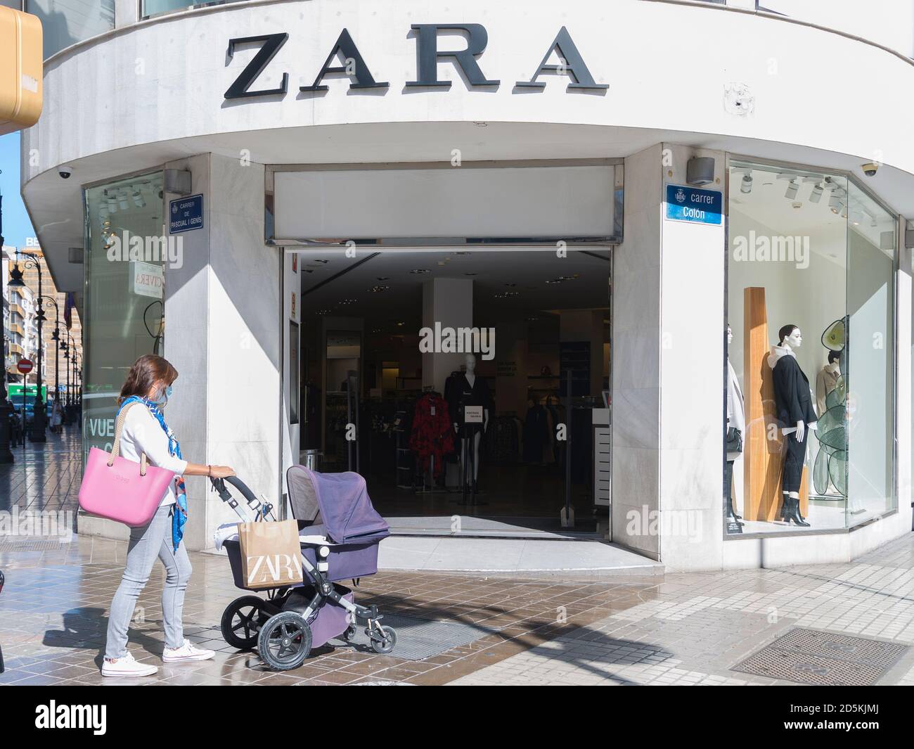 Una mujer que lleva una máscara con un carro para bebés y una bolsa de  compras Zara pasa por la tienda Zara Fotografía de stock - Alamy