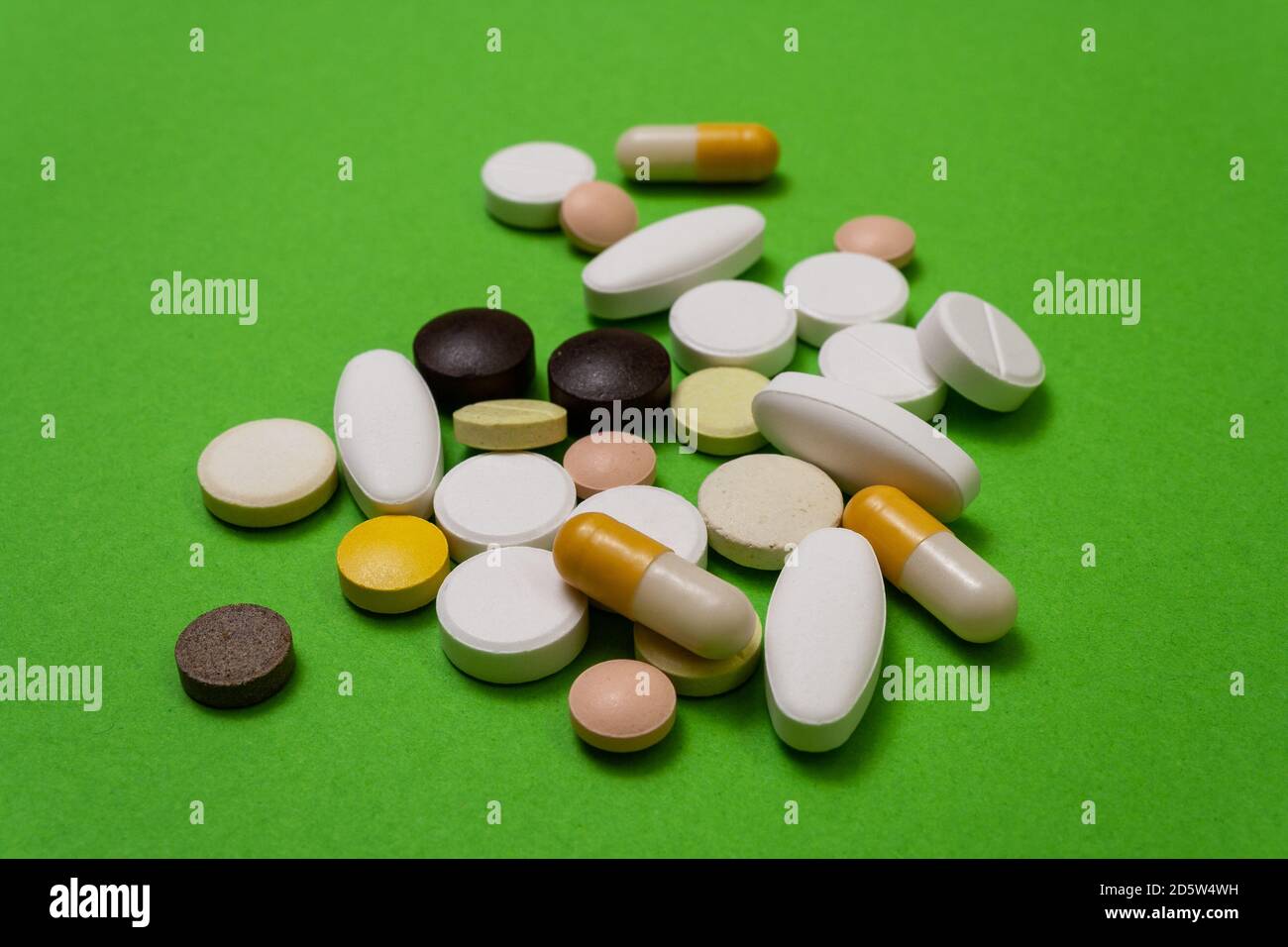 Muchas píldoras redondas de colores y cápsulas sobre fondo verde de la mesa de cerca, tabletas de macroinyección, medicamentos pandémicos aislados. Medicamentos enfermedad tratantes Foto de stock