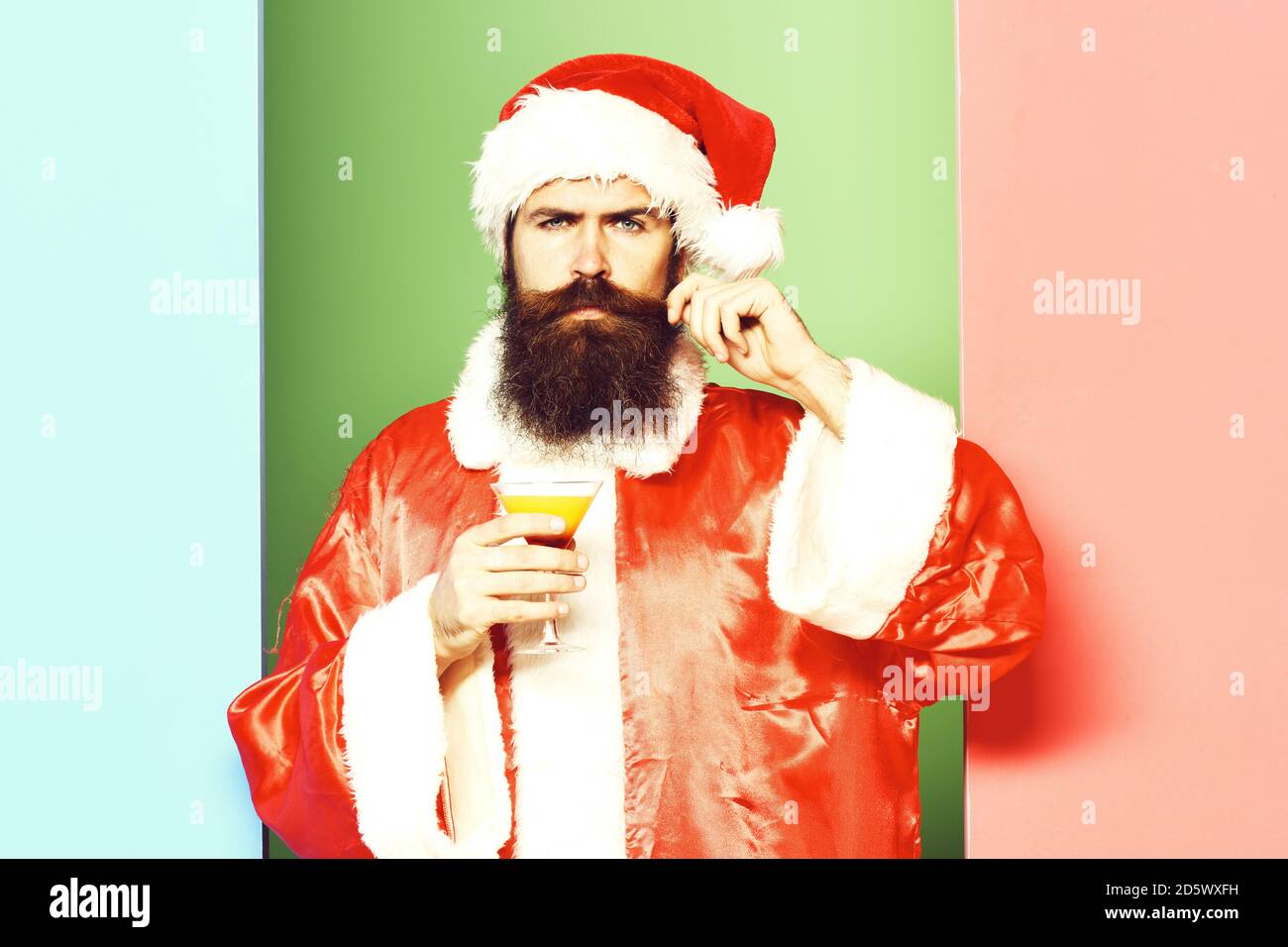 Guapo barbudo santa claus hombre con barba larga en serio sosteniendo un  vaso de bebida alcohólica en navidad o suéter de Navidad y Año Nuevo  sombrero. En coloridos fondo studio Fotografía de
