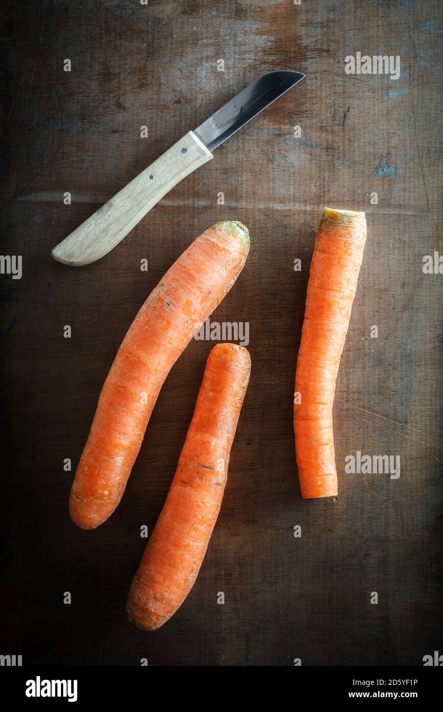 Tres zanahorias y un cuchillo de cocina en madera oscura Foto de stock
