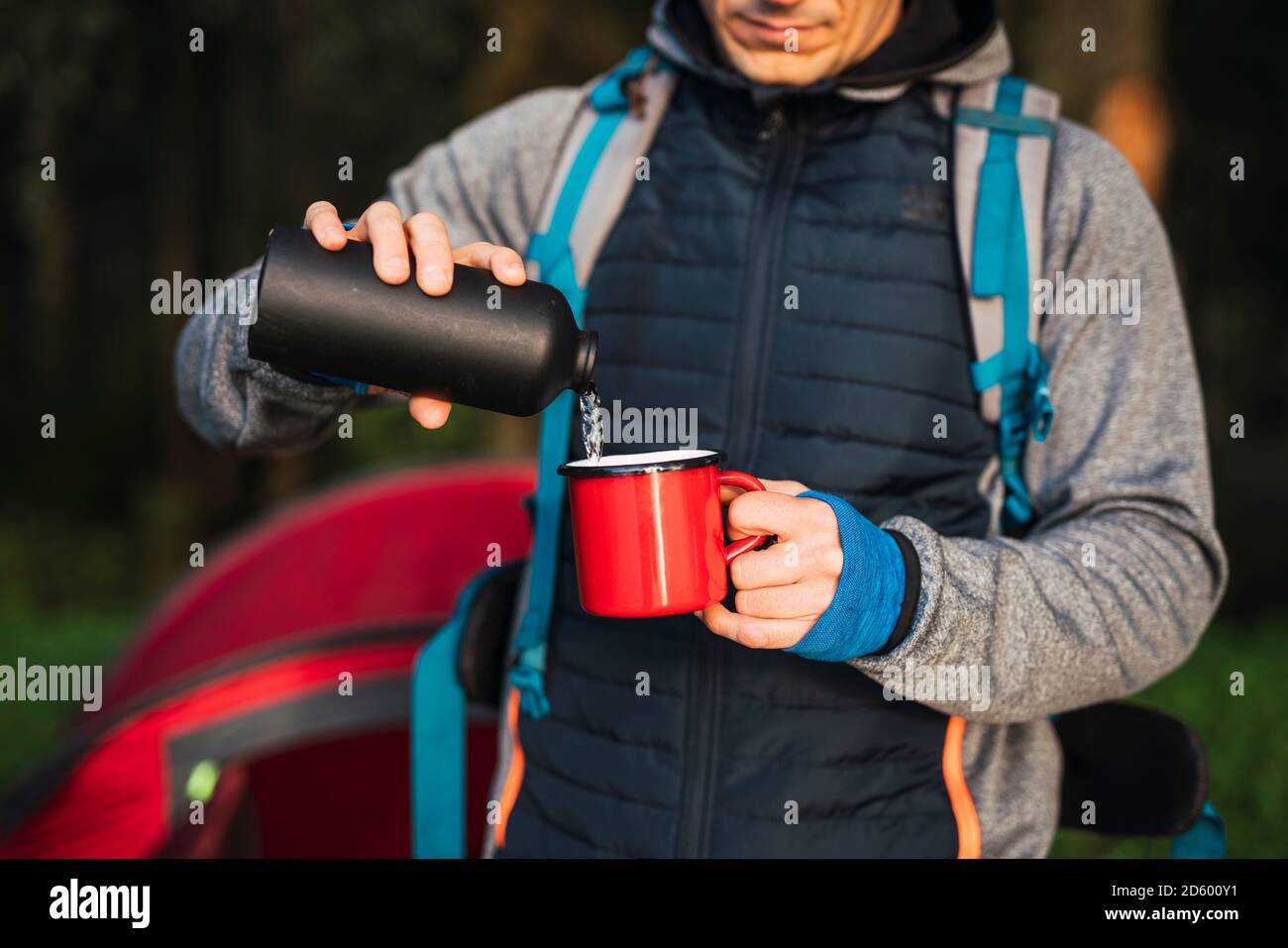 Hombre acampando en Estonia, vertiendo agua en una taza Foto de stock