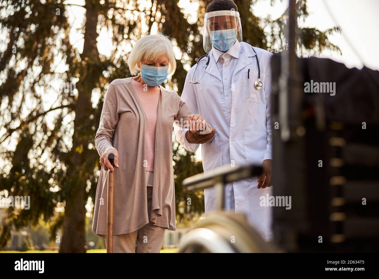 Un médico cauteloso que lleva a una mujer envejecida a una silla de ruedas Foto de stock