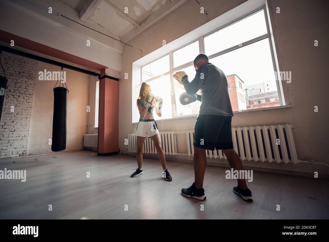 Un hombre y una mujer que escatiman compañeros se entrenan en el sala de entrenamiento de combatientes en guantes de boxeo con patas Foto de stock