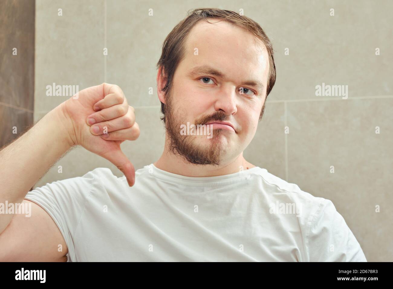 Un hombre adulto con media barba apunta tristemente un dedo hacia abajo. El  concepto de arreglo personal y problemas con la apariencia cuando se aísla  del coronavirus epid Fotografía de stock -