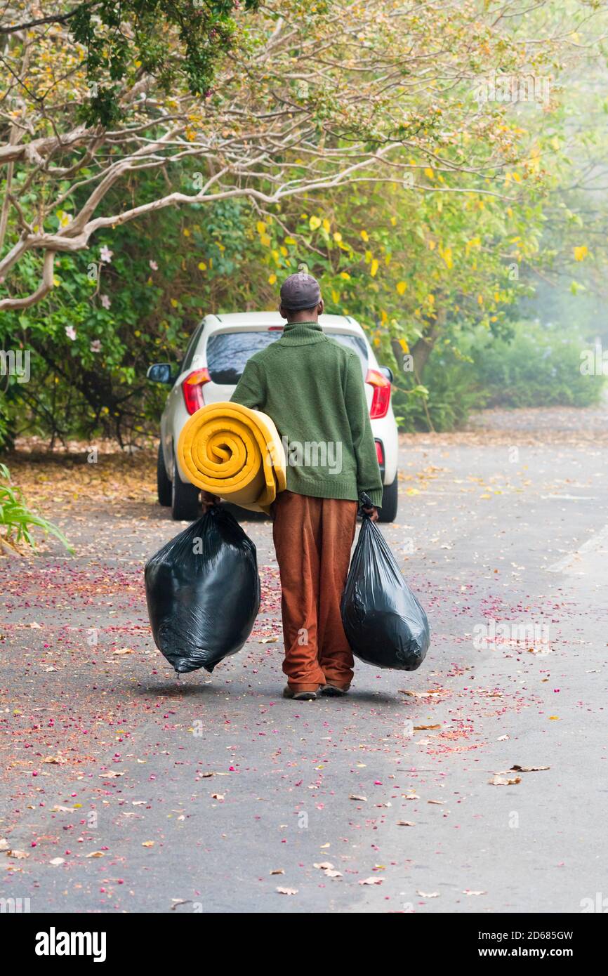 Un hombre africano sin hogar o indigente camina por la calle llevando sus posesiones en bolsas concepto de pobreza, penuria, vida cotidiana en África Foto de stock