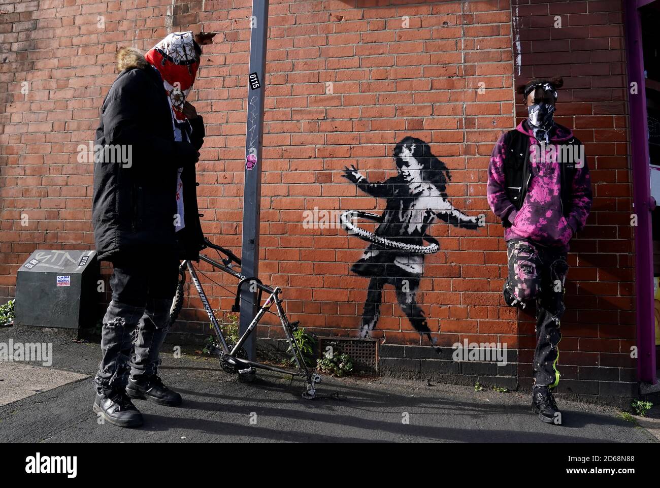 Residentes de Nottingham Paris Hendrix (izquierda) y Phidizz al lado de las obras de graffiti, ahora confirmado como obra del artista callejero Banksy, en un lado de una propiedad en Rothesay Avenue y Ilkeston Road, Nottingham. La obra de arte representa a una niña jugando con un neumático y está pintada en una pared cerca de una bicicleta abandonada que falta una rueda. Foto de stock