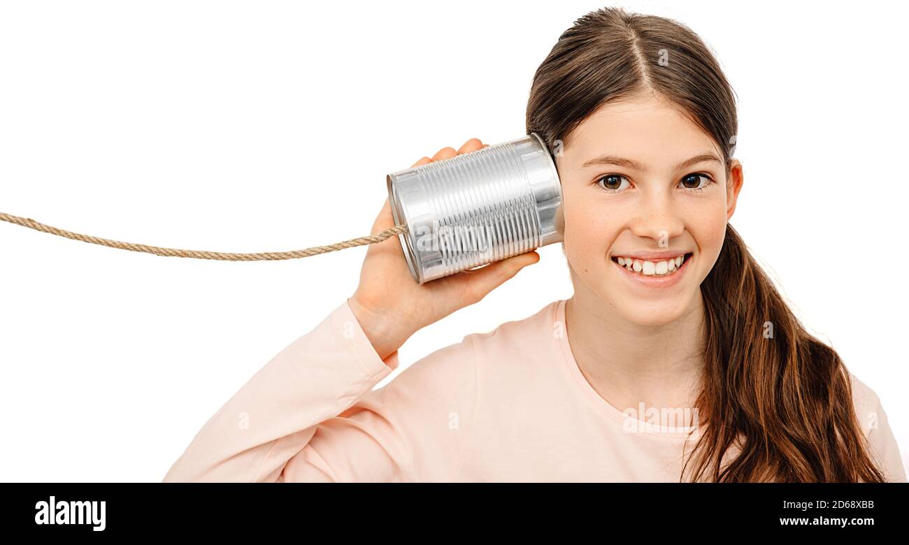 Una chica positiva con una lata cerca de la oreja, tocando el teléfono. Te oigo bien, niño aislado en blanco Foto de stock