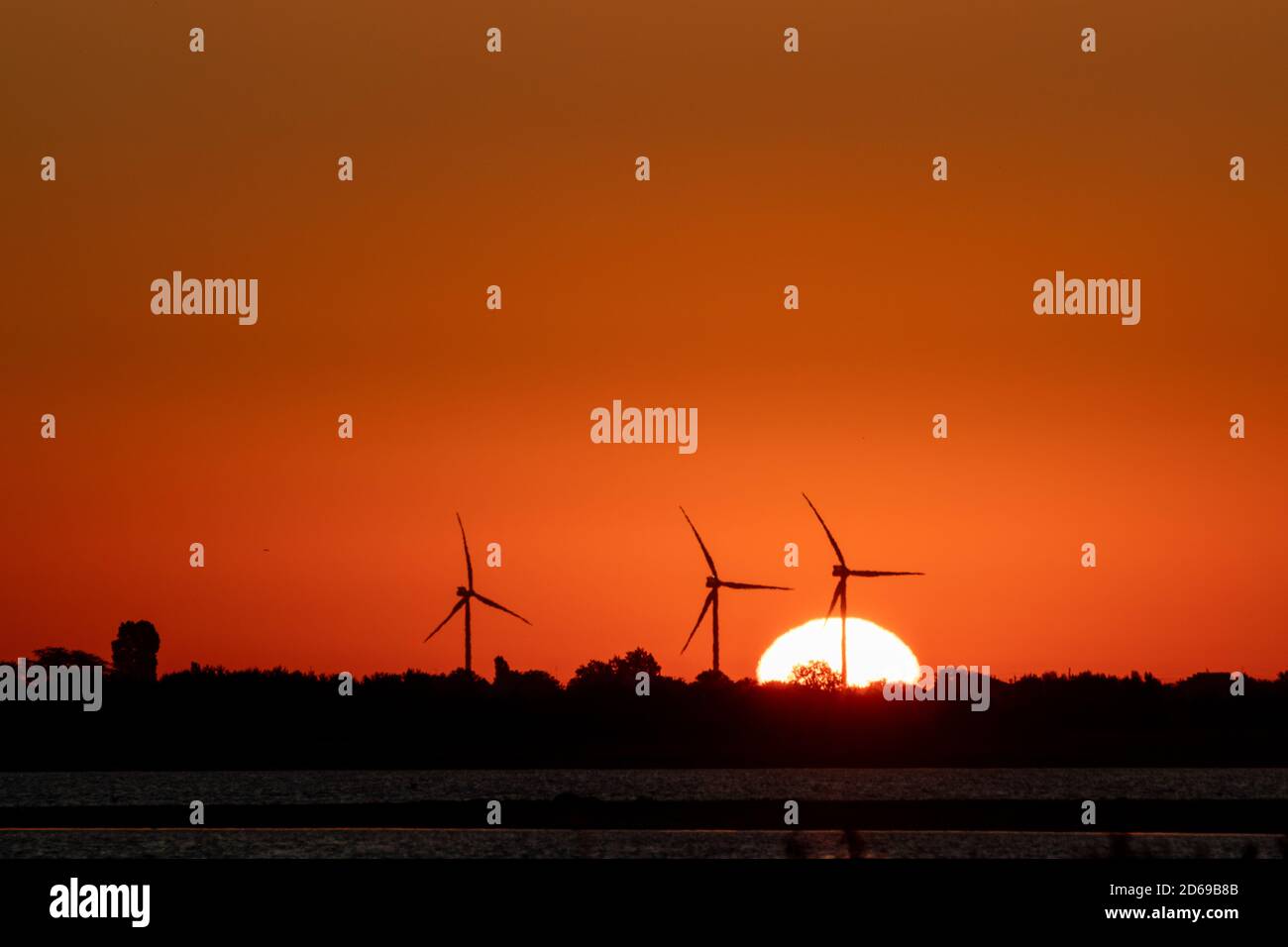 Generadores de viento granja silueta en el amanecer rojo naranja vibrante cielo y gran sol en ascenso. Turbinas de energía industria sostenible Foto de stock