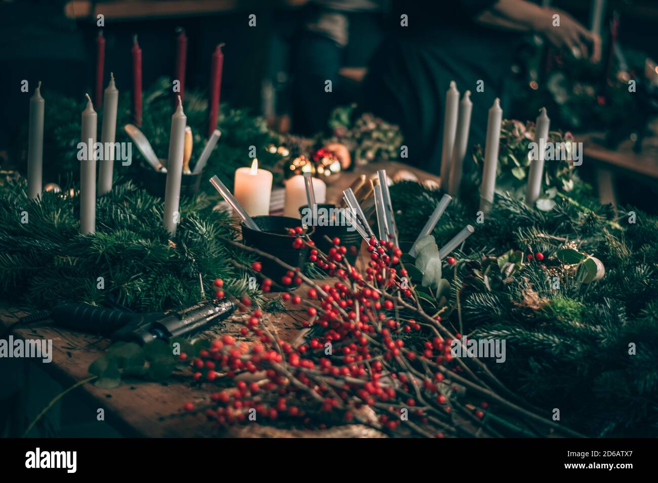 bayas rojas, pegamento, tijeras, vela ardiente y ramas verdes componentes  en la mesa mientras que hace coronas de adviento Fotografía de stock - Alamy