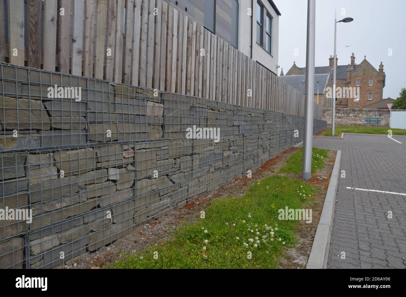 Un muro arquitectónico compuesto por unidades de gaviones de malla de alambre embalados en piedra junto a un aparcamiento en Escocia. Foto de stock