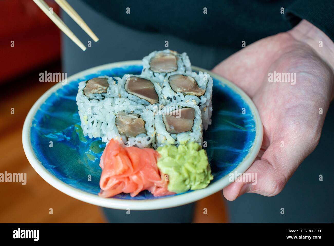Un pequeño plato de porcelana azul de sushi con palillos de madera que se sostiene en la mano de un macho. Foto de stock