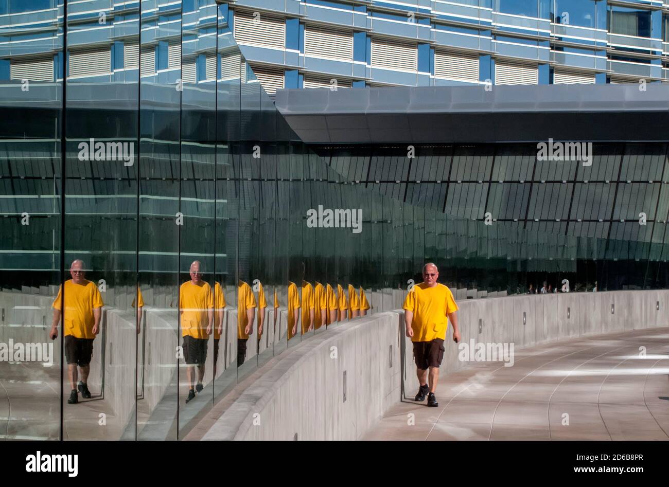 Hombre en camisa amarilla reflejada en las ventanas mientras camina en una calle de la ciudad Foto de stock