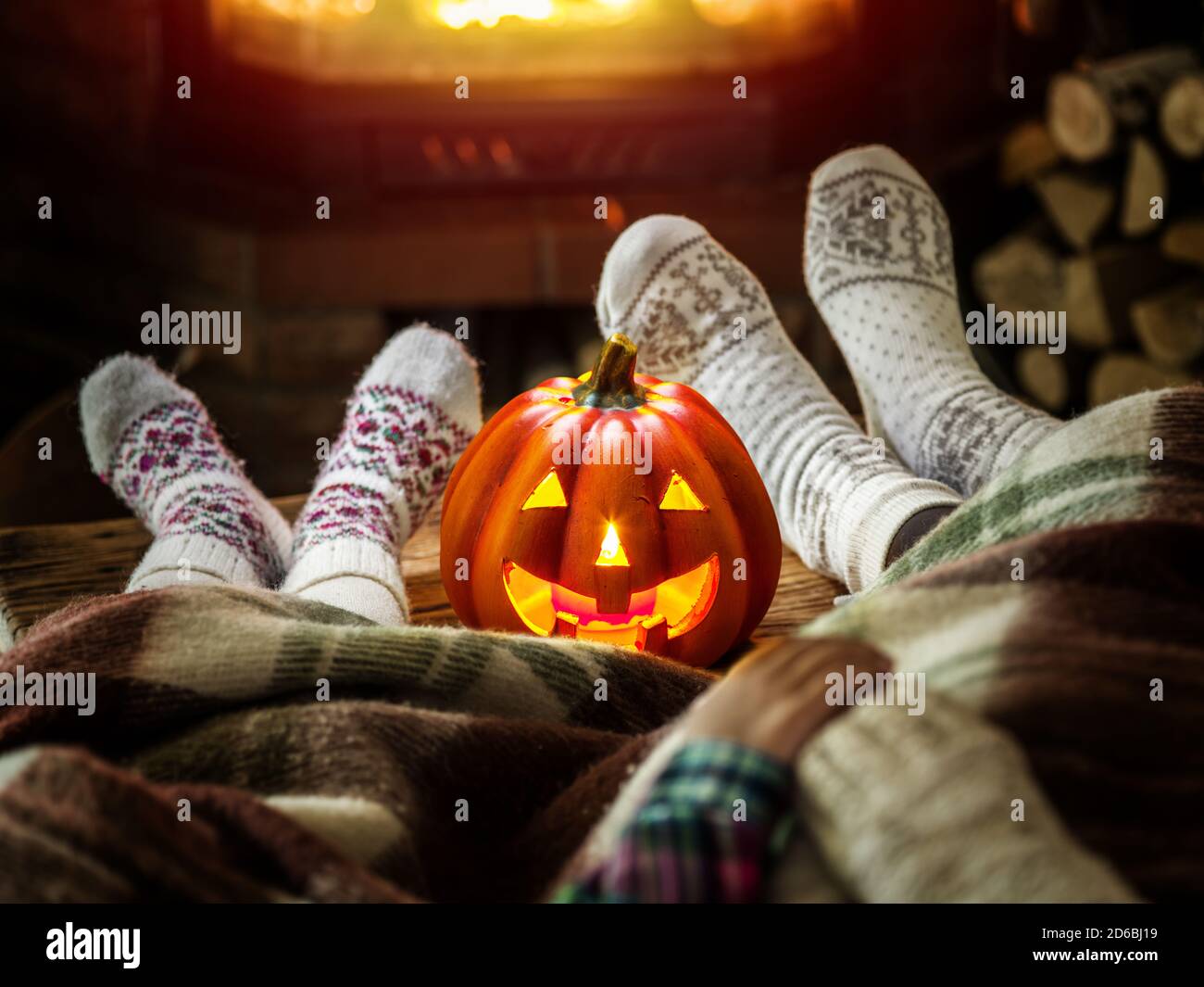 Los pies femeninos y infantiles están en calcetines de lana suave con chimenea de fuego en el fondo. Celebración de Halloween. Tallando la calabaza jack-o-linterna está en Foto de stock