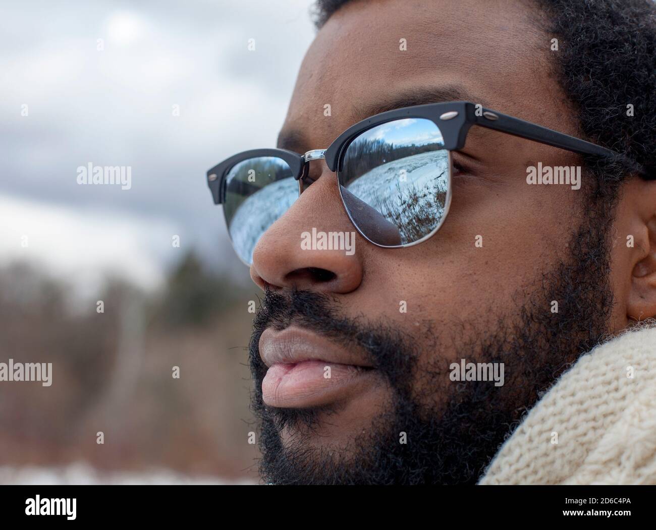 Un hombre con gafas de sol de estilo hacia fuera sobre un pantano congelado, reflejado en las lentes de sus gafas, en un día de invierno en Ithaca, NY Fotografía