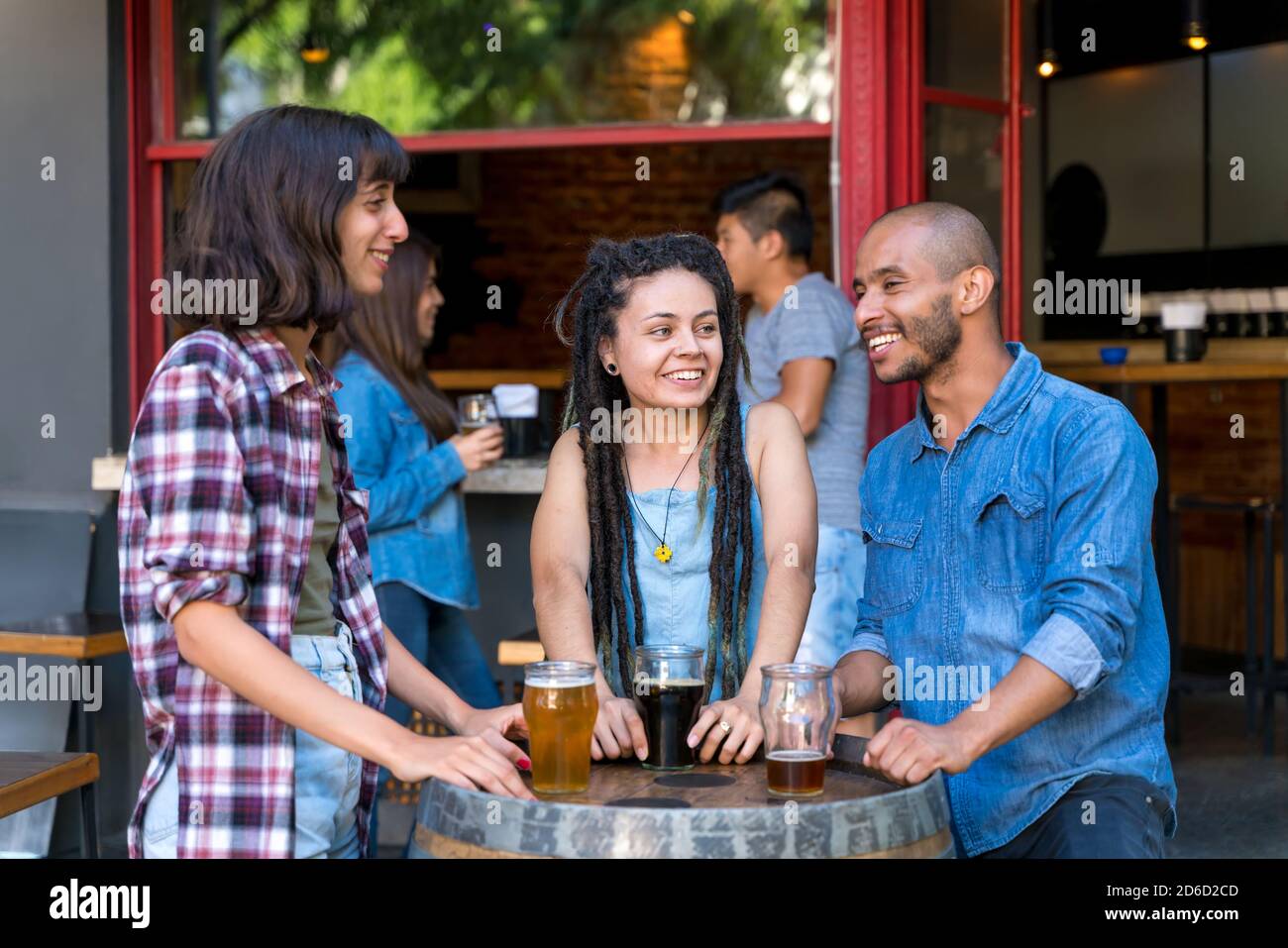 Un grupo de amigos de pie al aire libre en un barril de cerveza mientras que toma bebidas y charla de la diversión. Foto de stock