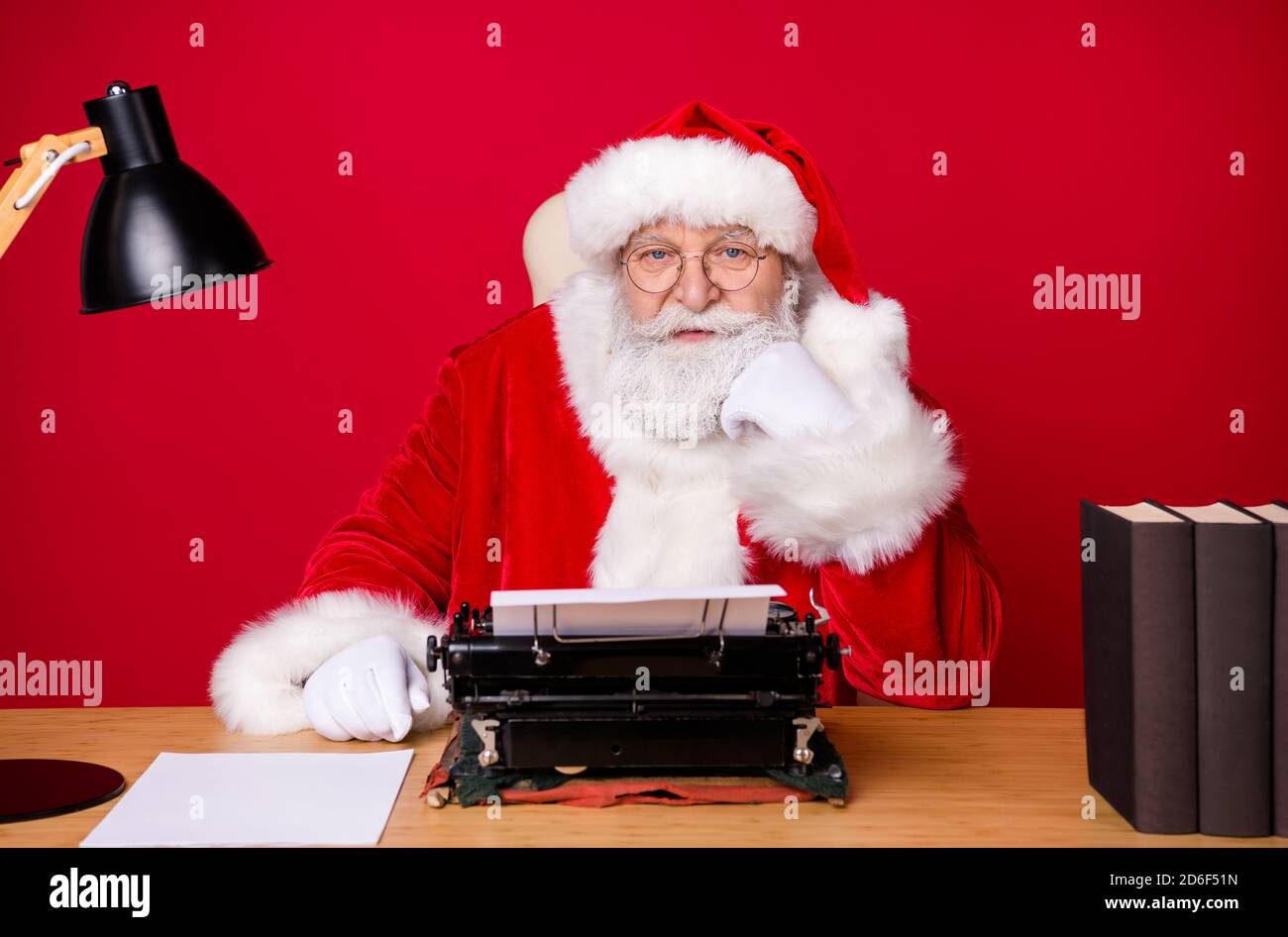 Foto de santa claus barba gris Siéntese la mejilla del puño del escritorio  tipwriter vintage lámpara libro de papel ropa x-mas disfraz abrigo gorra  gafas aisladas de color rojo Fotografía de stock -