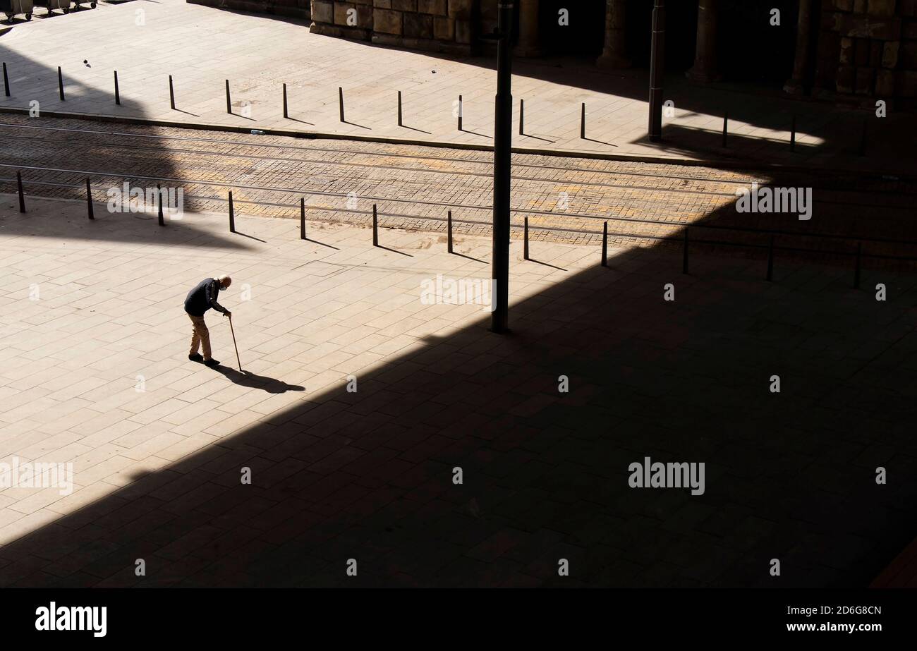 Belgrado, Serbia - 09 de octubre de 2020: Silueta de un hombre viejo caminando lentamente con un bastón a través de la plaza de la ciudad hacia la sombra oscura, en vista de gran ángulo Foto de stock