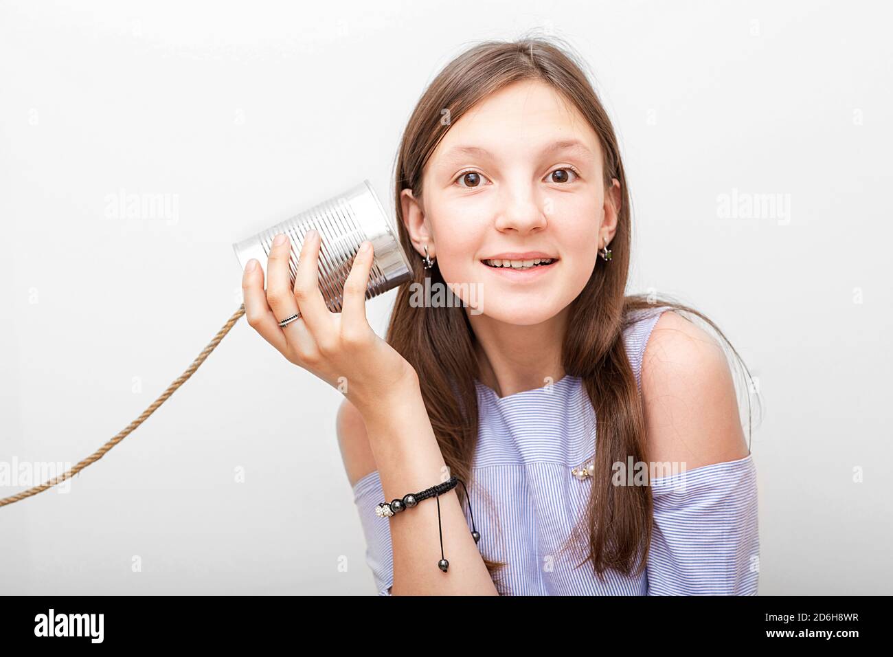 Una chica positiva con una lata de lata de teléfono cerca de la oreja, jugando en retro conectado chat. Te oigo bien, niño aislado en blanco Foto de stock