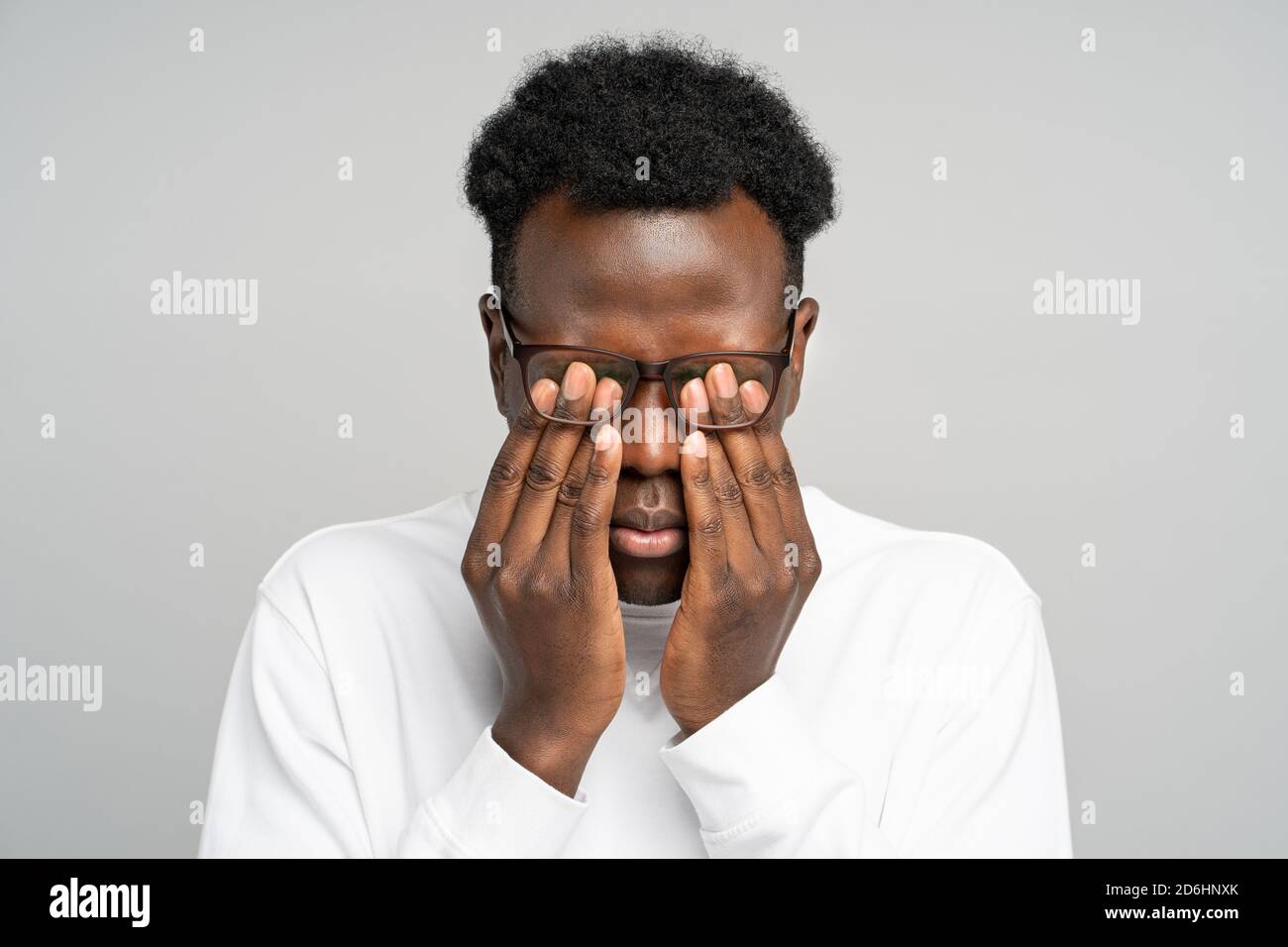 Primer plano de un joven afroamericano soñoliento con gafas frotándose los ojos, se siente cansado después de trabajar en el portátil, aislado sobre fondo gris. Exceso de trabajo, TI Foto de stock