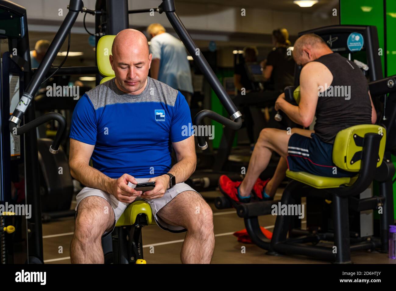Hombre mirando el teléfono en el gimnasio con equipo de ejercicio, centro deportivo North Berwick, East Lothian, Escocia, Reino Unido Foto de stock