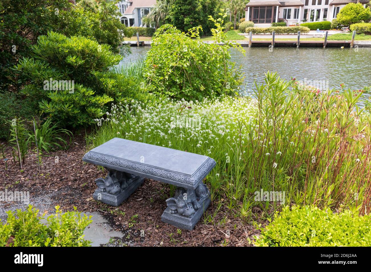 Un jardín de Carolina del Sur en mayo. Hierba estrella blanca delante de un banco de piedra al lado de un canal. Foto de stock