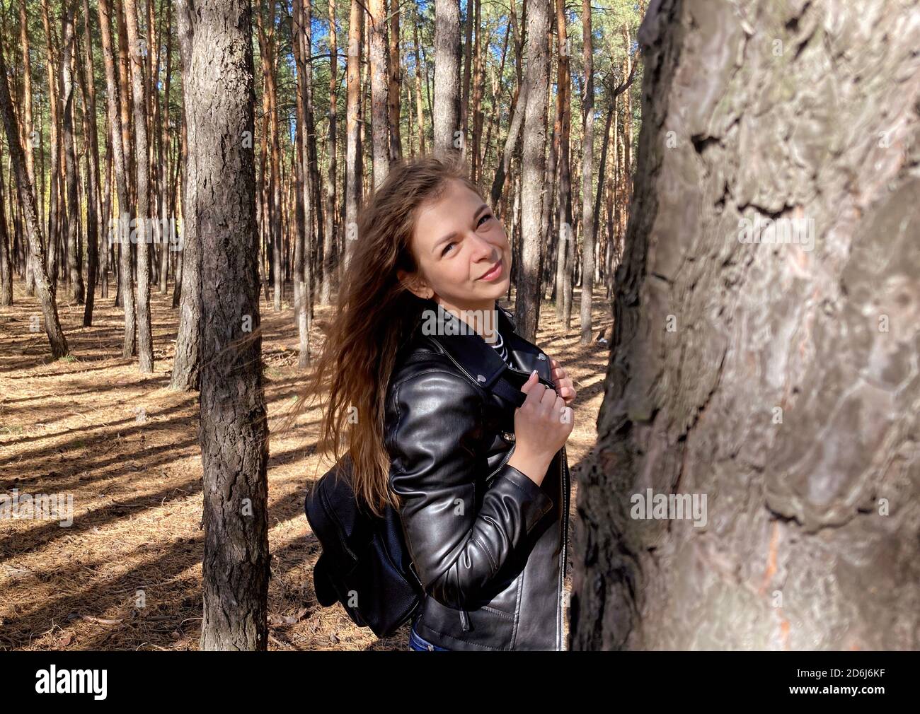 Primer plano de una joven atractiva posando en madera. Mujer encantadora fotografiada a cámara, de pie en el bosque. Foto de stock