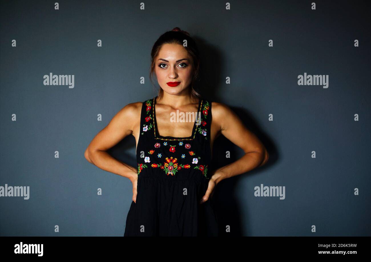 Joven mujer étnica con elegante vestido negro con tradicional mexicano  bordado floral de colores que se pone de pie sobre la pared oscura  Fotografía de stock - Alamy