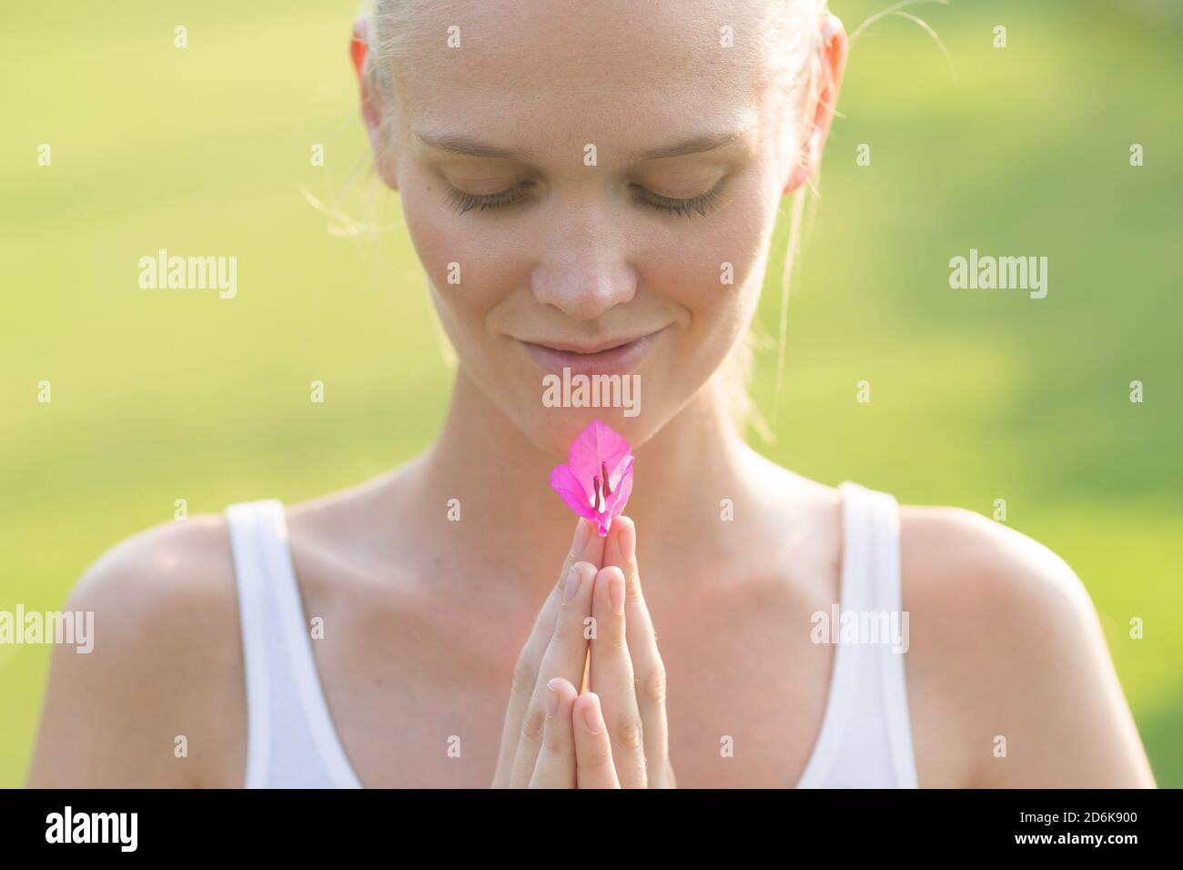 Bienestar y relajación. Mujer joven tranquila sosteniendo una flor rosa en sus manos contra un fondo verde. Foto de stock