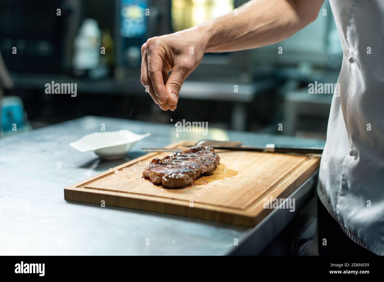 Mano del chef rociando especias en el bistec de ternera asado durante preparación Foto de stock