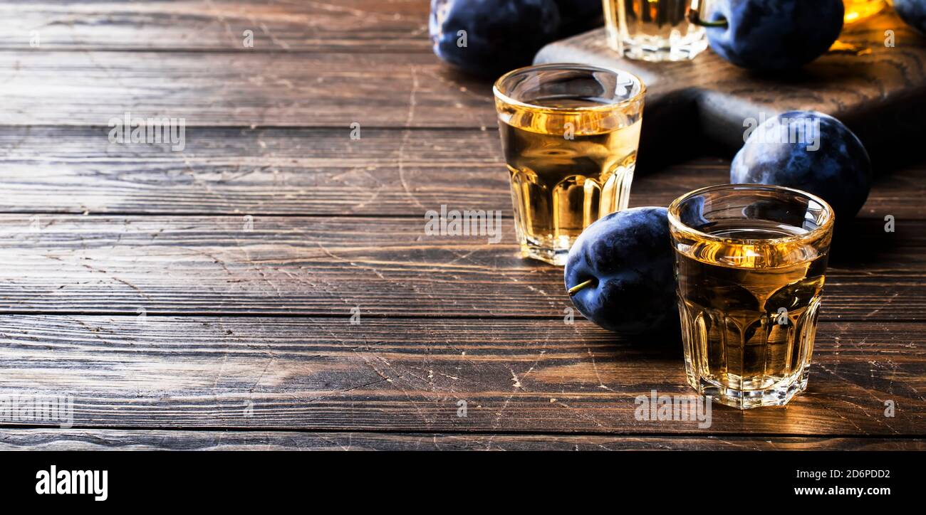 Slivovica - brandy de ciruela o vodka de ciruela, licor fuerte, bebida fuerte en vasos en la vieja mesa de madera, ciruelas frescas, espacio de copia Foto de stock