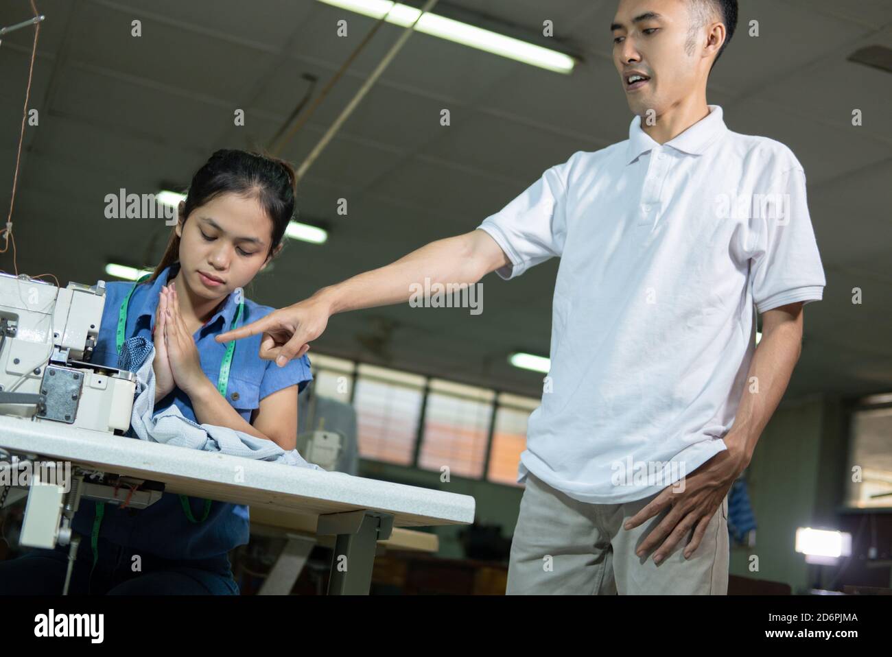 el supervisor masculino con una mano señalante reprides a un sastre femenino por cometer un error Foto de stock