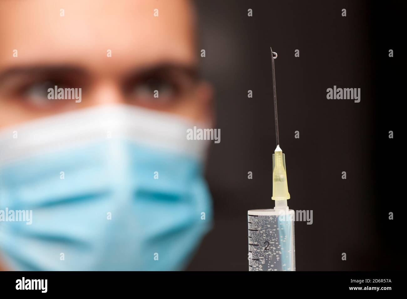 Primer plano del médico con mascarilla médica para la preparación de una jeringa vacunación - enfoque en la aguja Foto de stock