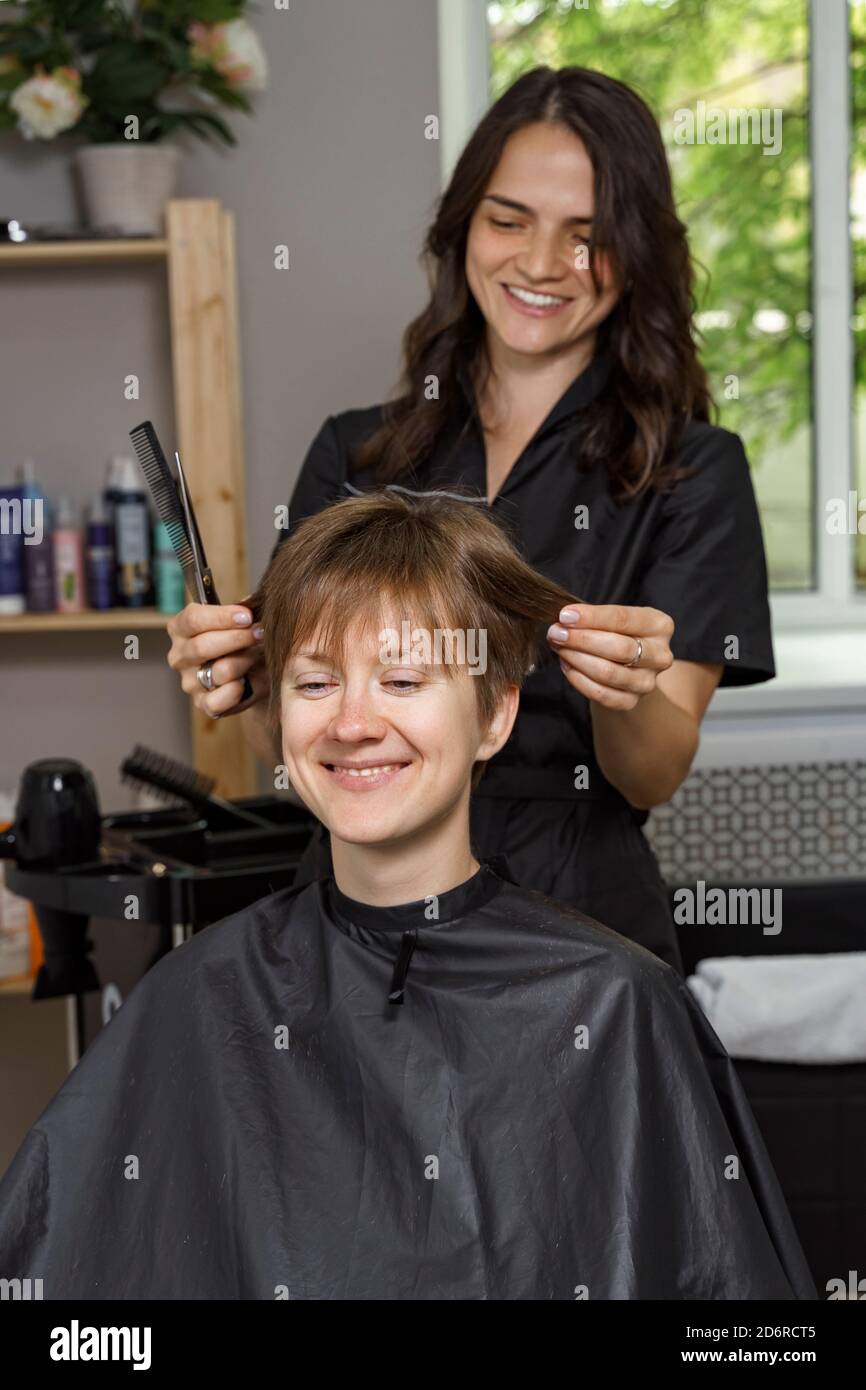 hermosa mujer peluquera en uniforme negro corta el pelo de mujer joven. concepto de belleza Fotografía de stock - Alamy