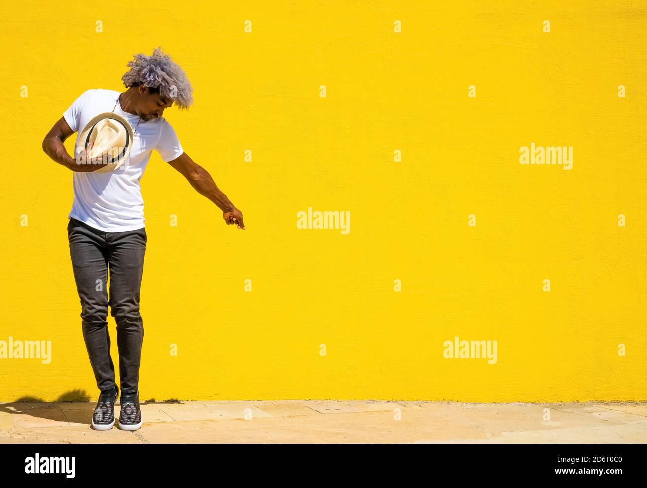Hombre negro con pelo afro y sombrero bailando sobre un fondo amarillo. Bailando con un sombrero. Foto de stock