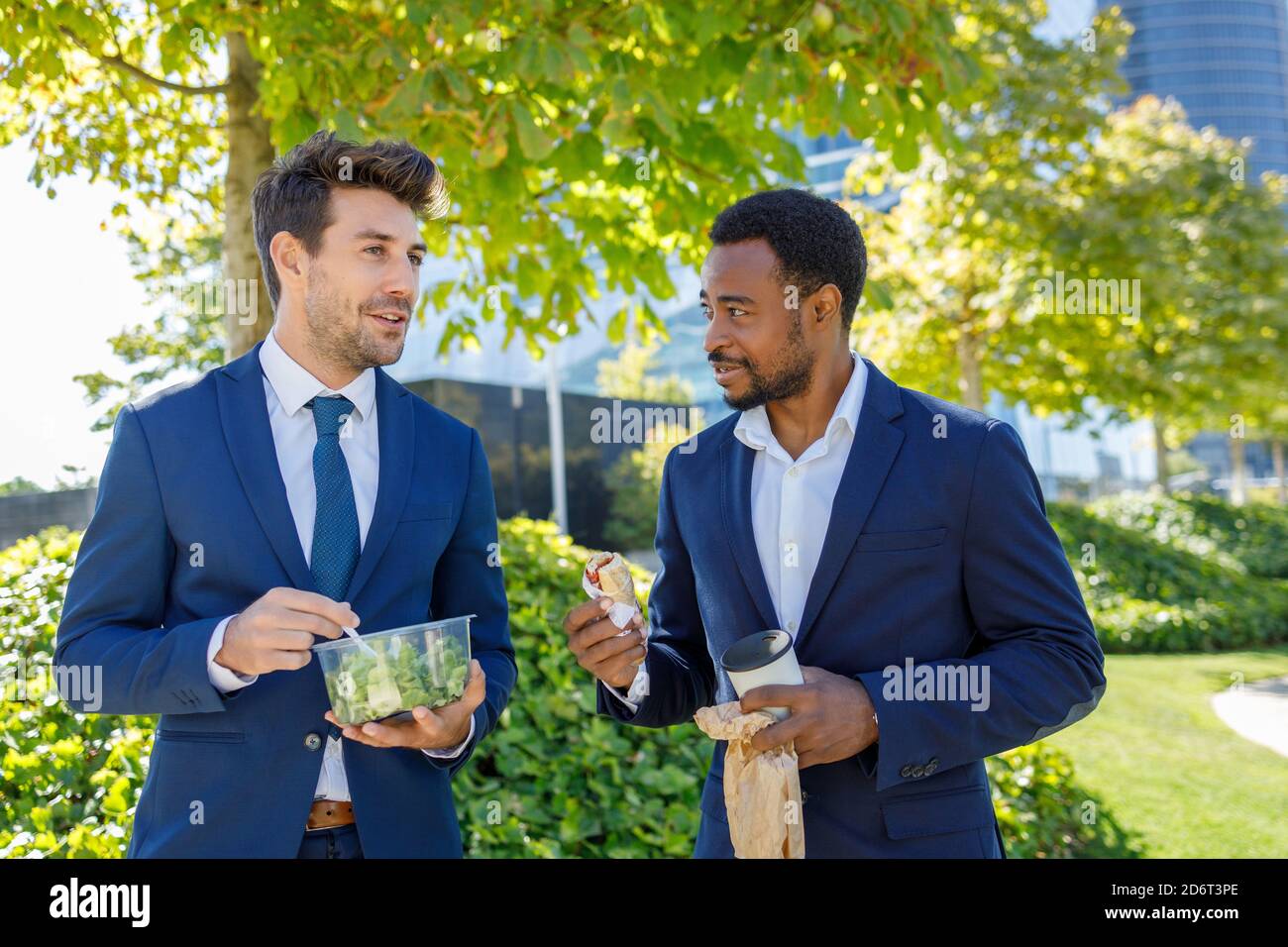 Positivo jóvenes diversos compañeros de trabajo en ropa formal sonriendo  mientras que teniendo almuerzo juntos en la calle en el día soleado  Fotografía de stock - Alamy