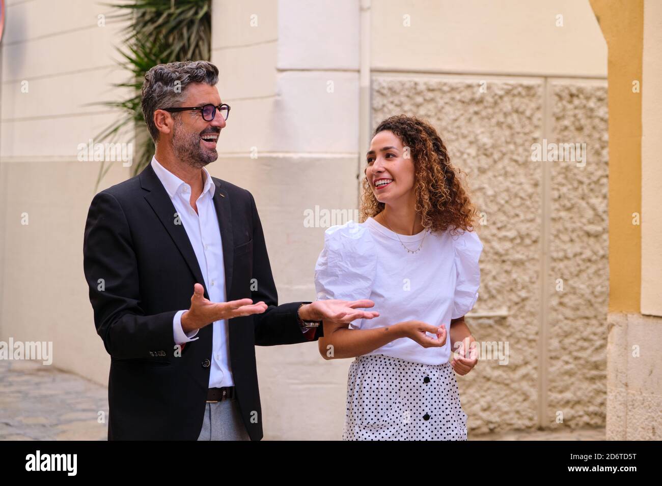 Hombre maduro y mujer étnica joven con ropa informal elegante hablar entre  sí mientras camina por la calle antigua Fotografía de stock - Alamy