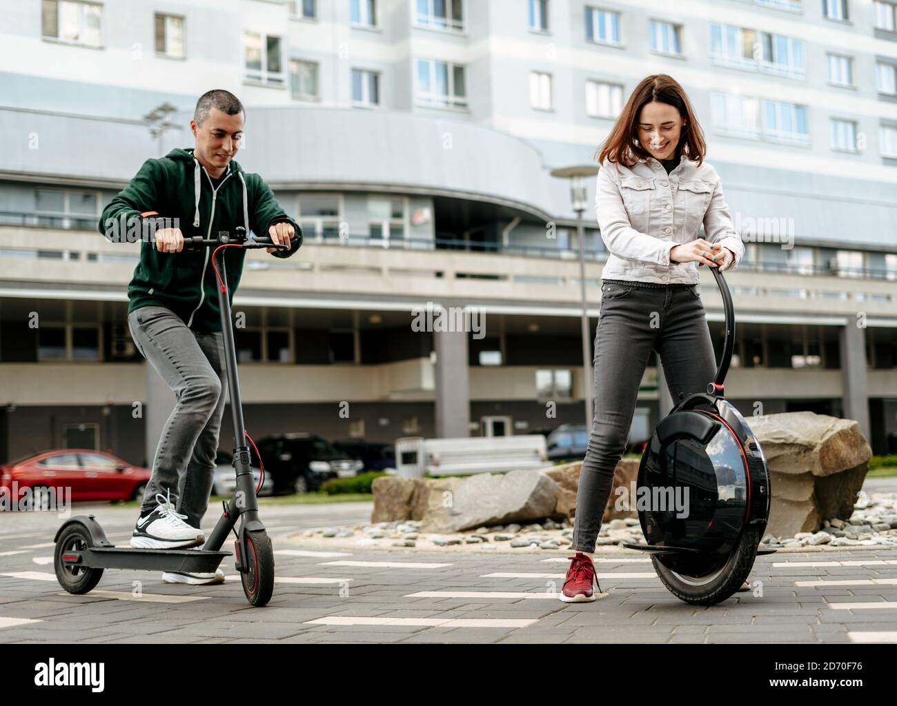 Joven hombre montando eléctrico patada scooter y mujer joven en ropa informal en moniciclo en la calle de la ciudad Foto de stock